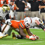 Notre Dame and Miami football players dive for a ball.